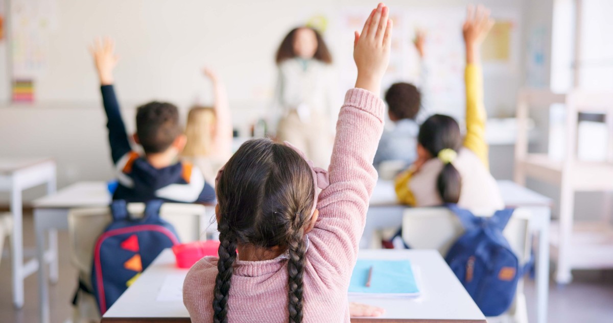 Education, raised hand and girl student in classroom with teacher for learning, discussion and knowledge.