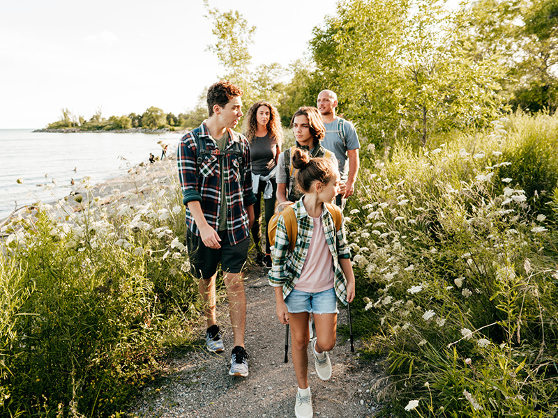 Caucasian family go walking at a lake with three children. Siblings in front of mom and dad walking and talking.