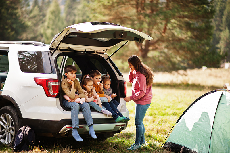 Family of four kids and mother at vehicle interior. Children sitting in trunk. Traveling by car in the mountains, atmosphere concept.