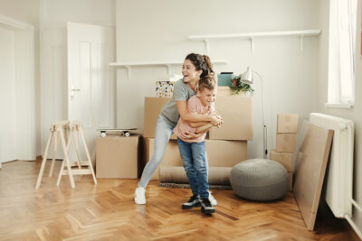 Happy Mother and Her Little Son Dancing in Room With Moving Boxes at New Home, Having Fun Enjoy Relocation in New House on Moving Day