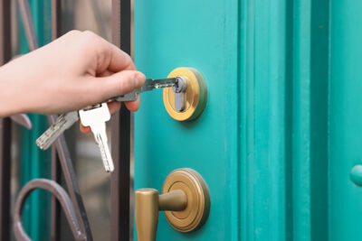 Woman opening door with key outdoors, closeup