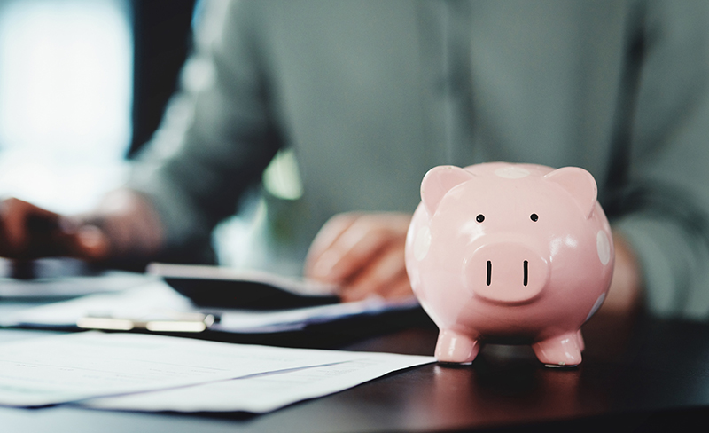 Shot of an unrecognizable businessman doing paperwork with a piggybank on his desk at work