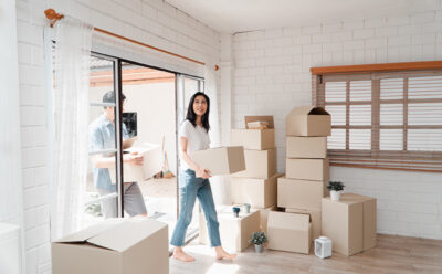 Happy young couple Carrying cardboard boxes and walking from the front door into the house in a new house at moving day. Concept of relocation, rental, and homeowner moving at home.