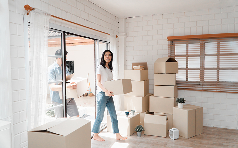 Happy young couple Carrying cardboard boxes and walking from the front door into the house in a new house at moving day. Concept of relocation, rental, and homeowner moving at home.